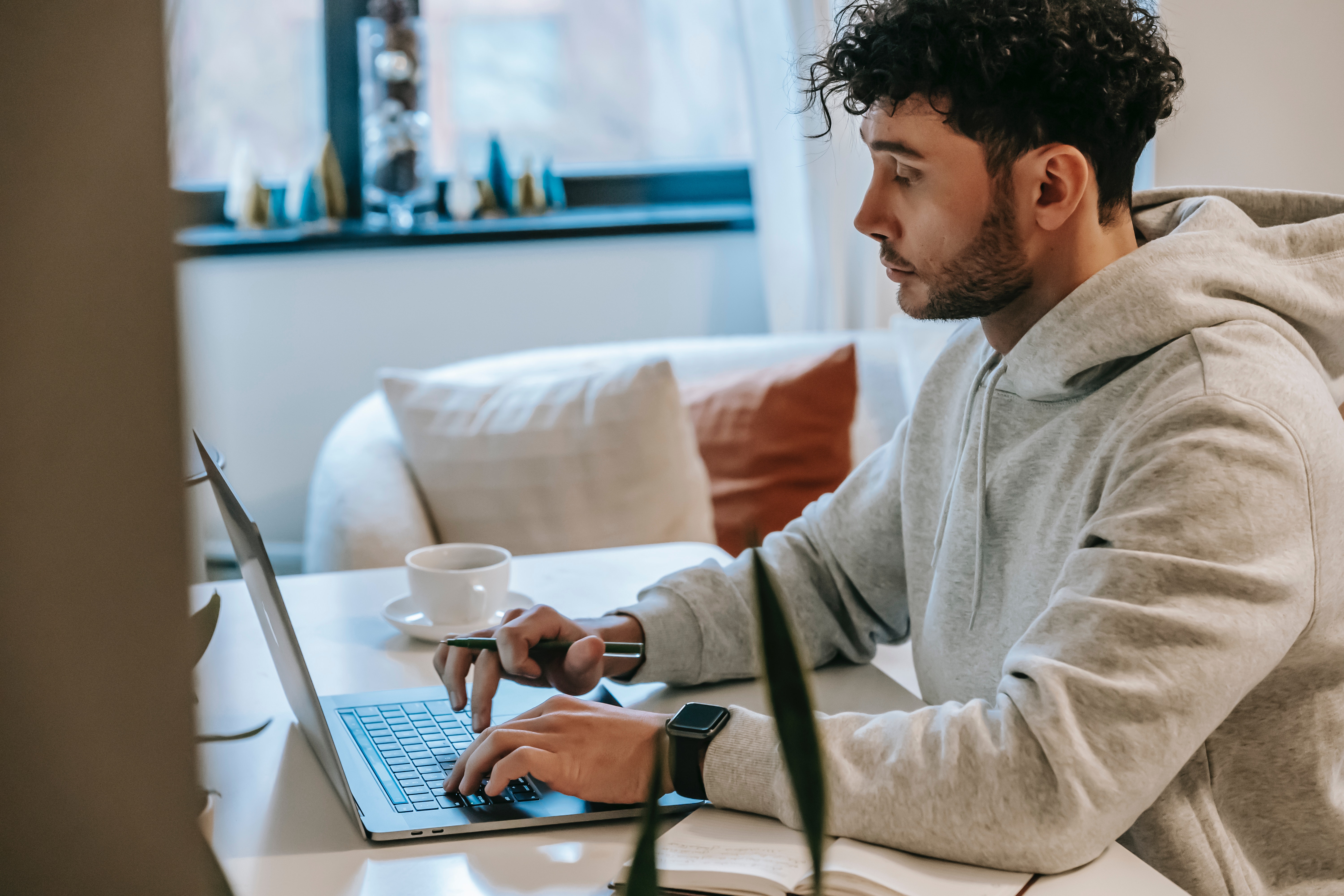 Homme en pull-over gris travaillant chez lui sur son ordinateur portable avec une tasse de café à côté de lui.