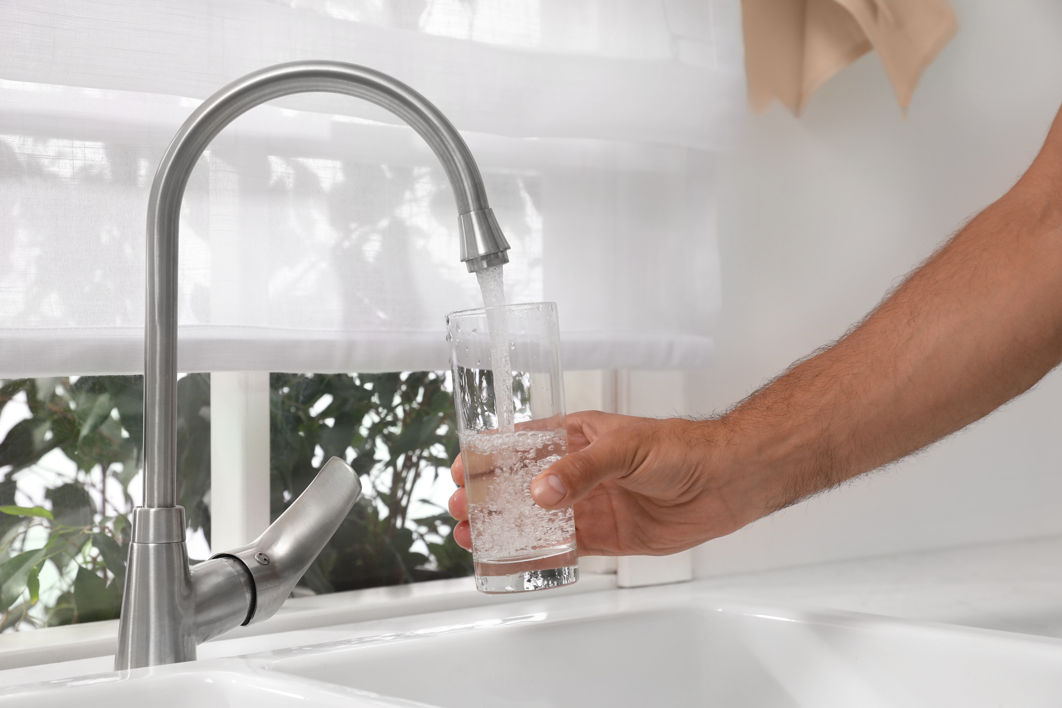 Een man giet kraantjeswater in een glas in een keuken