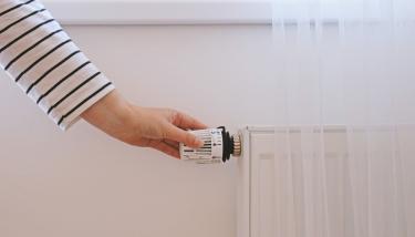 Une main règle le thermostat d'un radiateur